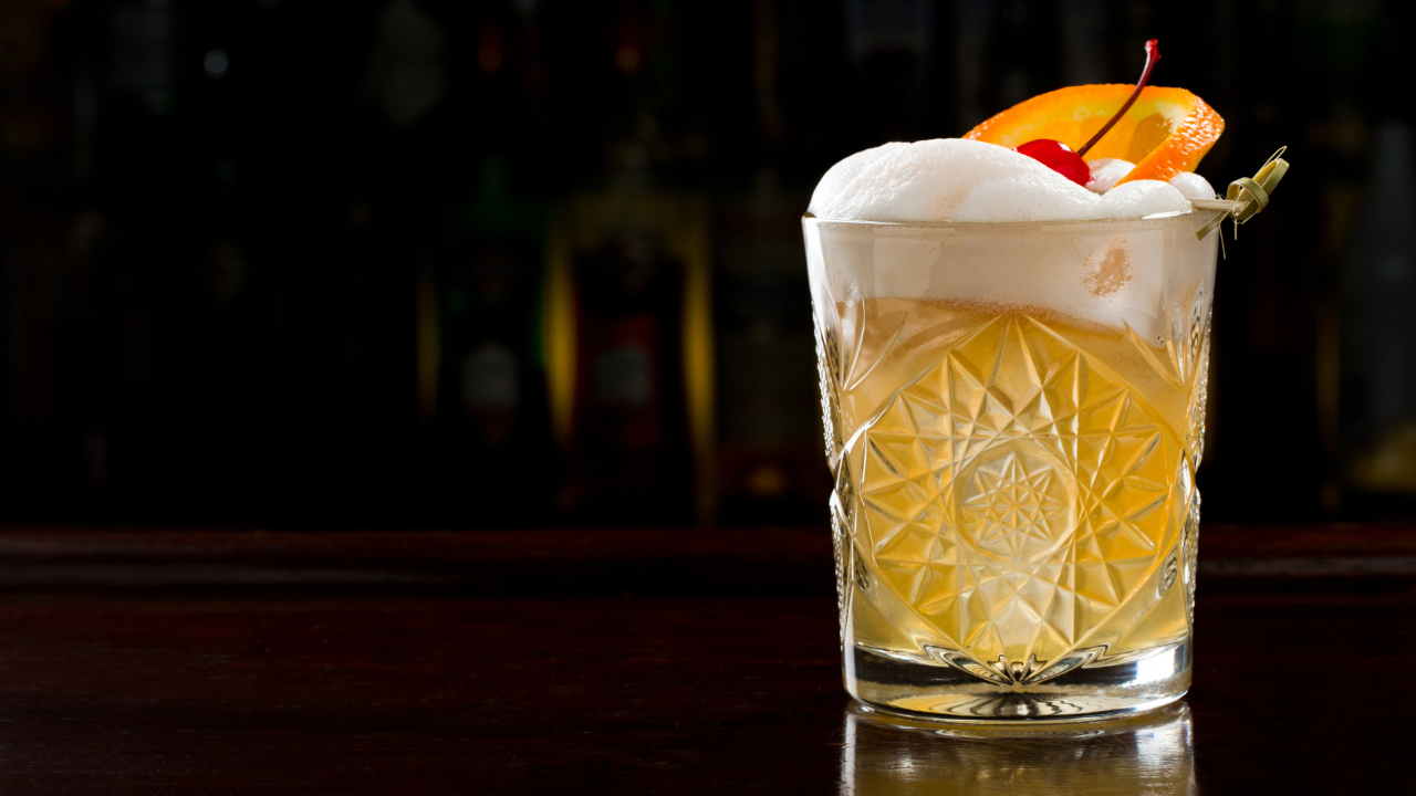 A Close up of a Whiskey Sour, one of the best bar drinks of 2024, in a fancy glass and dark background
