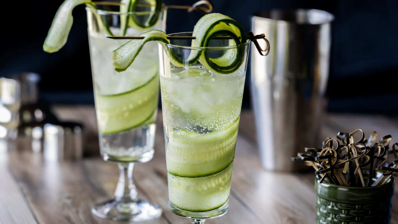 A close up of two elegant cocktails at a nice bar with cucumber ribbons and other garnishes