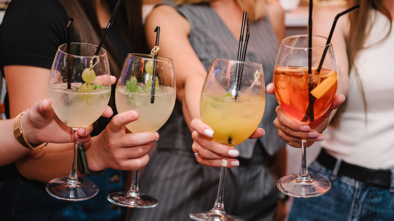 4 girls holding glasses of spirits with garnishes at a home bar