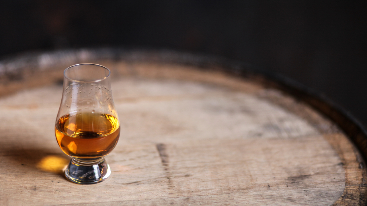 A closeup of a Glencairn glass of premium Bourbon for tasting on top of a barrel