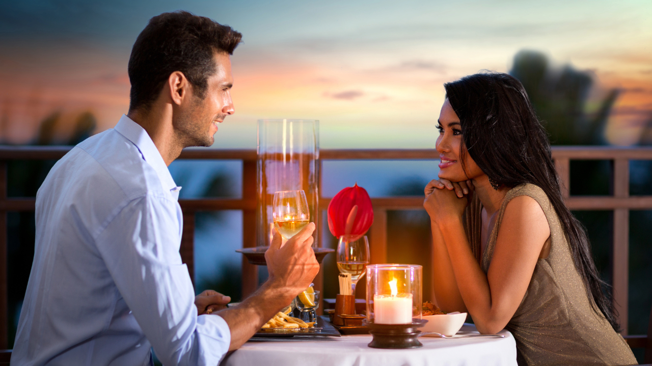 A couple with romantic drinks, flowers, and candlelight with a sunset in the background