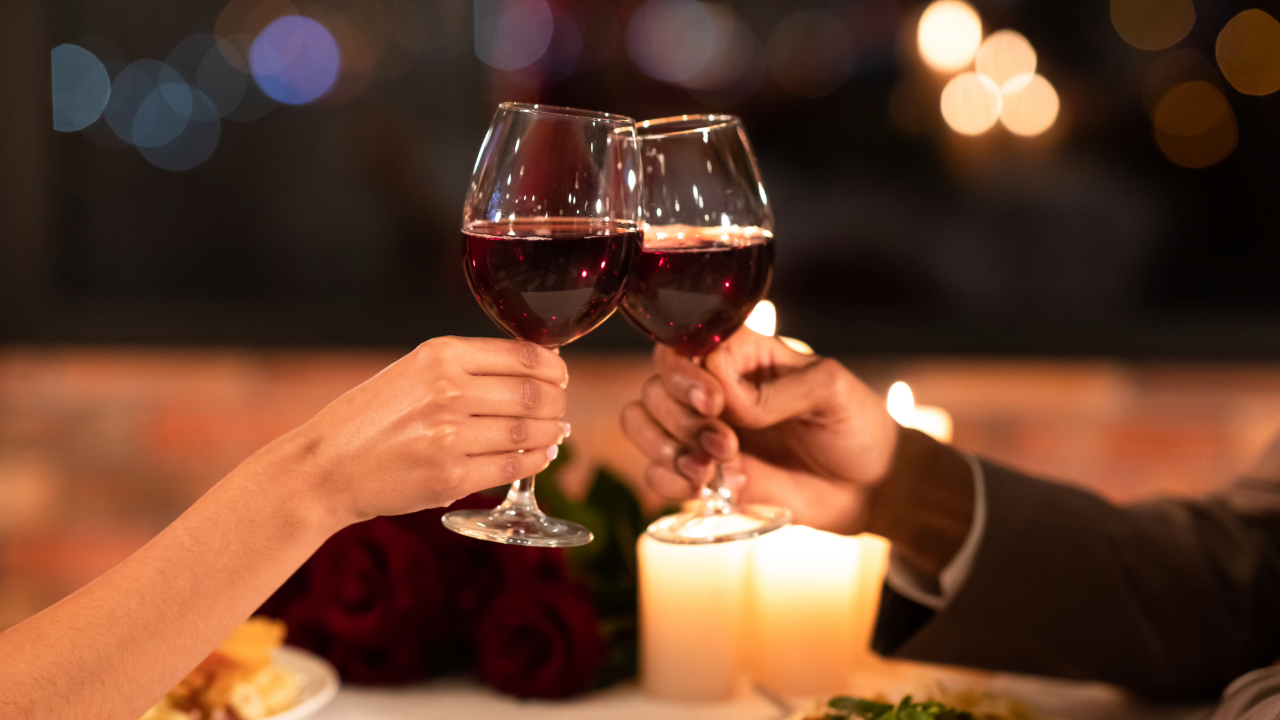 A romantic couple toasting with two drinks illuminated by candlelight