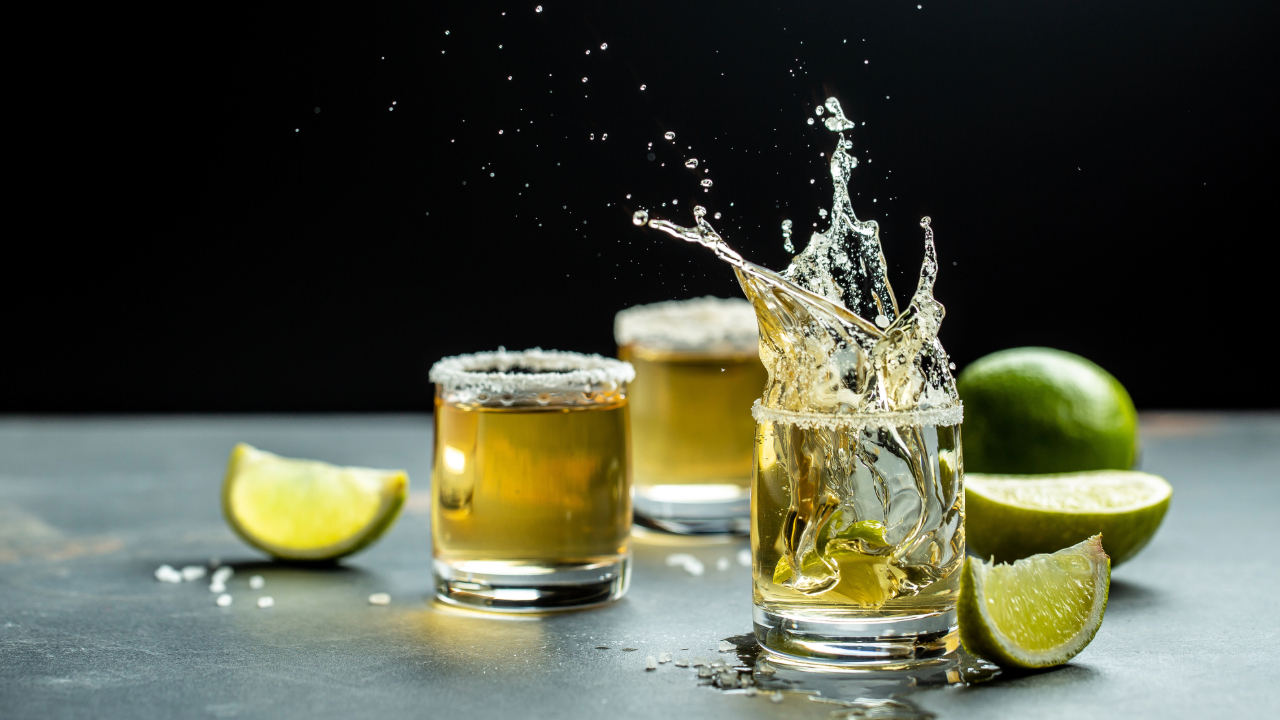 A shot of a lime splashing into a shot of tequila