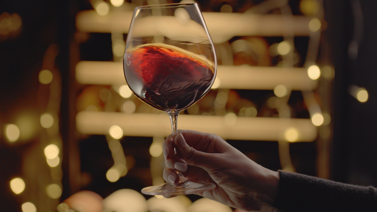 A pictured of a hand swirling red wine in front of a blurred christmas light background