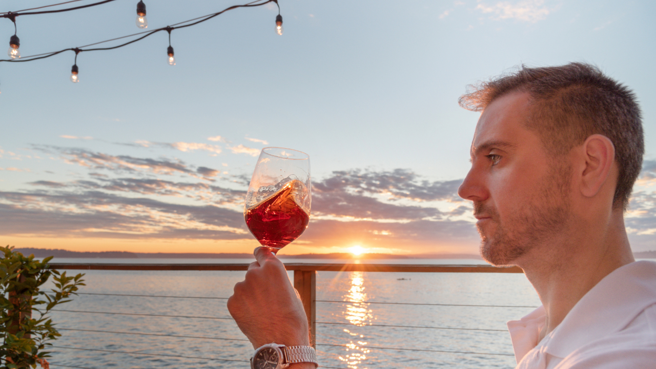 A man swirling premium wine in a glass overlooking a sunset